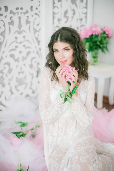 明るいスタジオでピオニーの花と白いレースのドレスで美しい若い女の子 — ストック写真