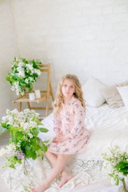 Leylak çiçekleri ile bir bahar stüdyosunda güzel bir elbise sarı saçlı sevimli küçük kız