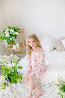 Leylak çiçekleri ile bir bahar stüdyosunda güzel bir elbise sarı saçlı sevimli küçük kız