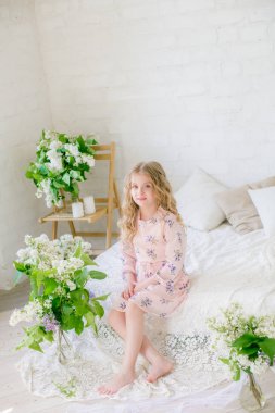 Leylak çiçekleri ile bir bahar stüdyosunda güzel bir elbise sarı saçlı sevimli küçük kız