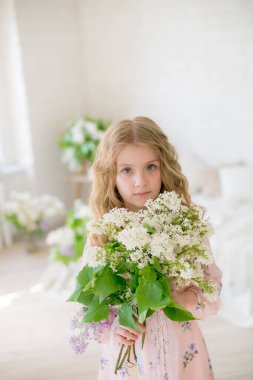 Leylak çiçekleri ile bir bahar stüdyosunda güzel bir elbise sarı saçlı sevimli küçük kız