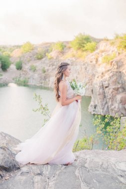 Güzel bir gölün kıyısında yaz aylarında bir buket ile gelinlik uzun saçlı güzel genç gelin