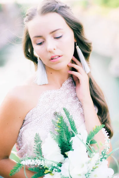 Beautiful young bride with long hair in a wedding dress with a bouquet in the summer on the shore of a beautiful lake