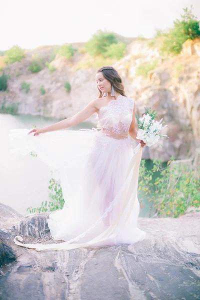 美しい湖のほとりに夏に花束を持つウェディングドレスで長い髪を持つ美しい若い花嫁 — ストック写真