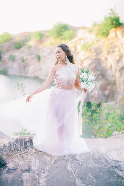 美しい湖のほとりに夏に花束を持つウェディングドレスで長い髪を持つ美しい若い花嫁 — ストック写真