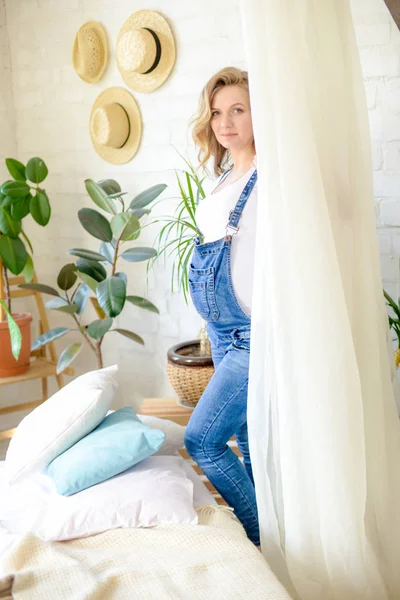 美丽的孕妇 穿着白色T恤和蓝色牛仔裤 在一个房间里有很多活的绿色植物 幸福母亲的概念 健康的生活方式 — 图库照片