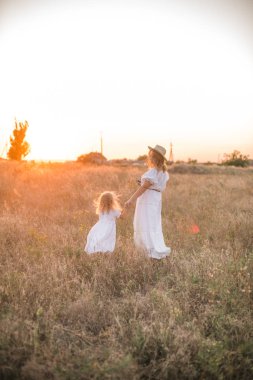Anne ve kızı elele ve günbatımı gökyüzü ile yeşil çayır tarafından arka plan üzerinde yürüme