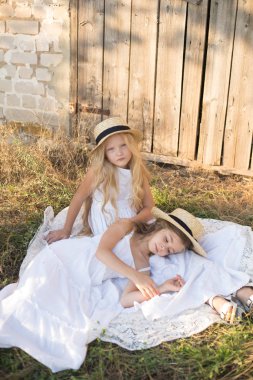 Bir hasır şapka ile beyaz elbiseler gün batımında bir yaz alanında sarı uzun saçlı sevimli küçük kızlar