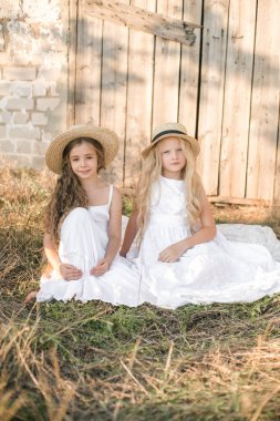 Bir hasır şapka ile beyaz elbiseler gün batımında bir yaz alanında sarı uzun saçlı sevimli küçük kızlar