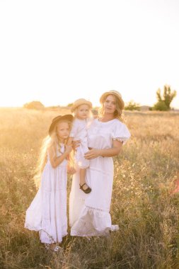 Yazın günbatımında kırsal bir alanda beyaz elbiseli, sarı saçlı genç bir anne.