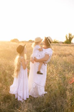Yazın günbatımında kırsal bir alanda beyaz elbiseli, sarı saçlı genç bir anne.