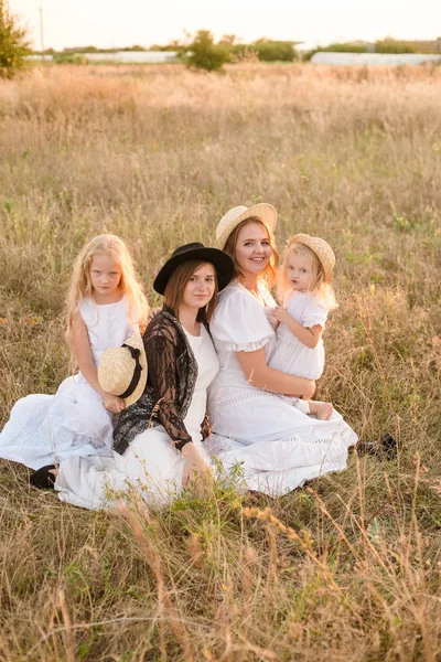 彼女の娘と田舎のフィールドで夏の日没時に白いドレスを着たブロンドの髪を持つ叔母と若い母親 フィールドで夏に同じ家族からのいくつかの女の子 — ストック写真