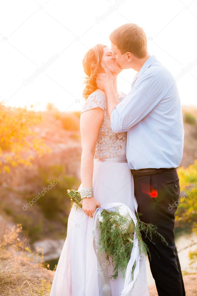 Elegant gentle stylish groom and bride near river or lake on sunset in summer. Wedding couple in love 