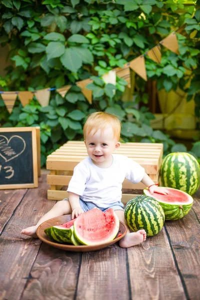 晴れた日に座って赤いおいしいスイカを食べて夏に金髪の小さな男の子 — ストック写真