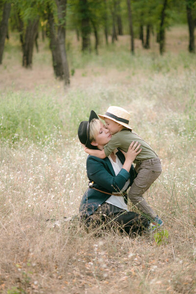 Little boy in a hat and his mom in the park in summer at sunset