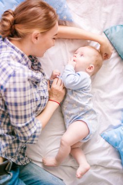Gömlek ve mavi jeans erkek bebek onun yatak - görüntü ile oynarken güzel anne portresi