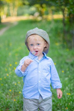 Çiçekli bir alanda yaz aylarında kap ve mavi gömlekli sarışın saçlı küçük çocuk