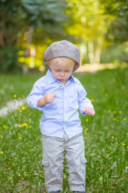 Çiçekli bir alanda yaz aylarında kap ve mavi gömlekli sarışın saçlı küçük çocuk
