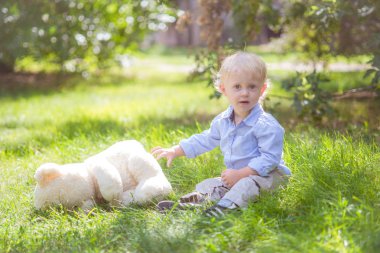 sarı saçlı bir oyuncak ayı yeşil çim ile yaz günde oynarken ile küçük çocuk
