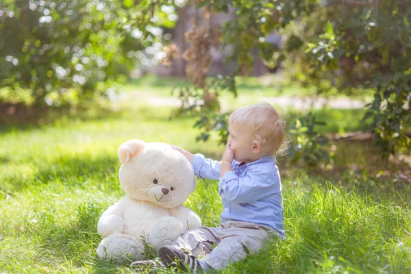 夏日绿草中与泰迪熊玩耍的金发小男孩 — 图库照片
