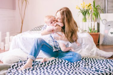 Gömlek ve mavi jeans erkek bebek onun yatak - görüntü ile oynarken güzel anne portresi