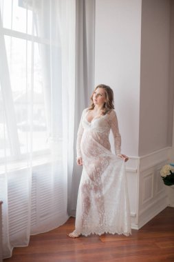 Genç güzel hamile kadın hamile bir kadının Göbek. Sevimli hamile göbeği. Beyaz dantel Peignoir güzel hamile kadın sarışın. Beyaz iç çamaşırı kız