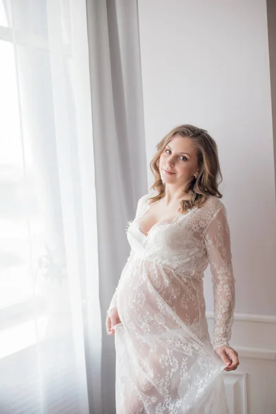 Young beautiful pregnant woman Belly of a pregnant woman. Cute pregnant belly. Beautiful pregnant woman blonde in white lace Peignoir. Girl in white lingerie