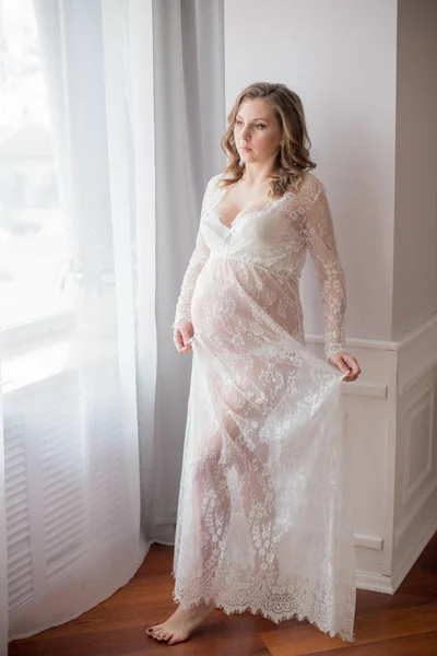 Young beautiful pregnant woman Belly of a pregnant woman. Cute pregnant belly. Beautiful pregnant woman blonde in white lace Peignoir. Girl in white lingerie