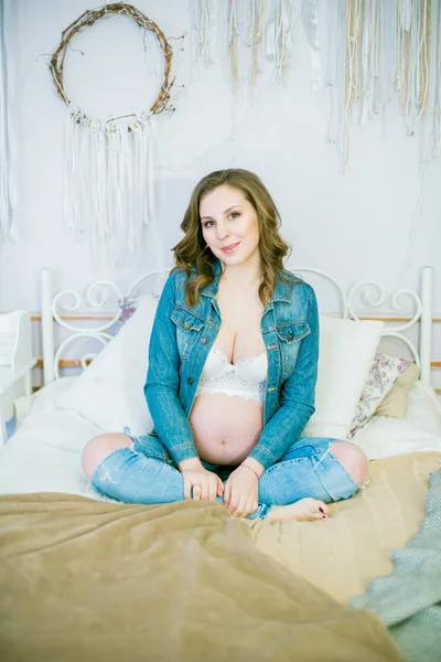 青いジーンズの美しい妊婦はベッドの上にあります 幸せな母性 健康的なライフスタイルの概念 — ストック写真
