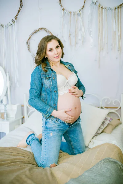美丽的孕妇穿着蓝色牛仔裤在床上 幸福母亲的概念 健康的生活方式 — 图库照片