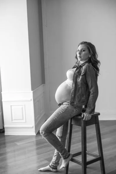 穿着蓝色牛仔裤和牛仔夹克的漂亮孕妇坐在高木椅上 幸福母亲的概念 健康的生活方式 — 图库照片