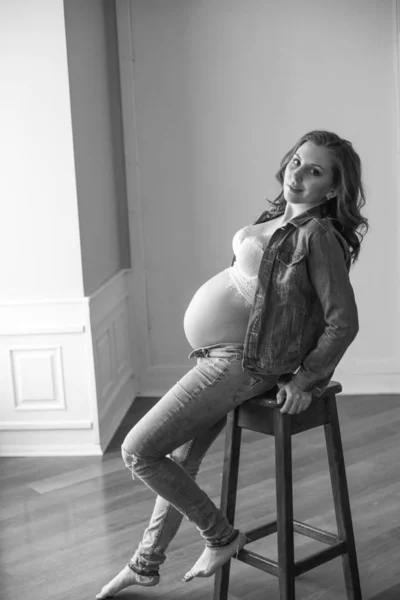 高い木製の椅子に青いジーンズとデニムジャケットの美しい妊娠中の女性 幸せな母性 健康的なライフスタイルの概念 — ストック写真