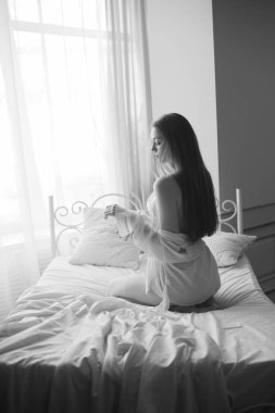 Siyah uzun saçlı sabah evde beyaz bir yatak beyaz dantel büstiyer ve elbise ile genç güzel gelin