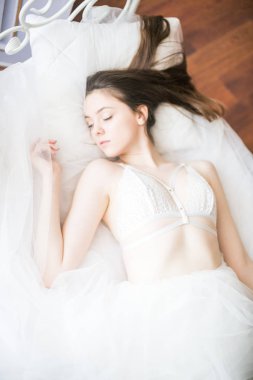 Siyah uzun saçlı sabah evde beyaz bir yatak beyaz dantel büstiyer ve elbise ile genç güzel gelin