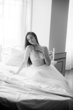 Siyah uzun saçlı sabah evde beyaz bir yatak beyaz dantel büstiyer ve elbise ile genç güzel gelin