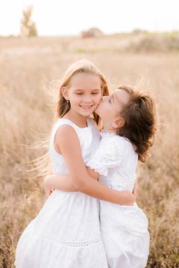 Bir hasır şapka ile beyaz elbiseler gün batımında bir yaz alanında sarı saçlı sevimli küçük kız kardeşler