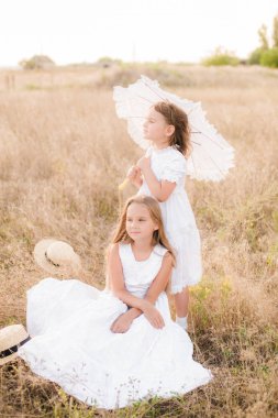 Bir hasır şapka ile beyaz elbiseler gün batımında bir yaz alanında sarı saçlı sevimli küçük kız kardeşler