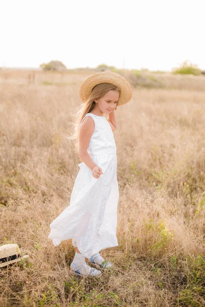 可爱的小女孩与金发在夏日田野在日落与一个白色的礼服与草帽 — 图库照片