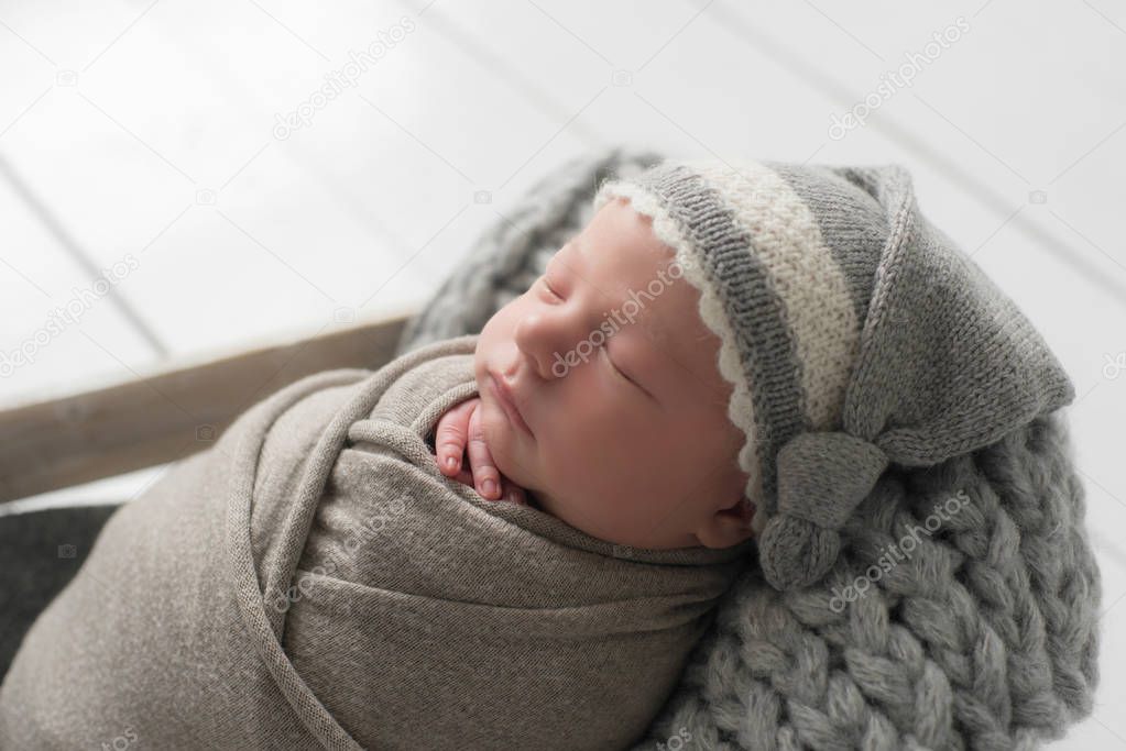 Sweet newborn baby sleeps in a basket. Beautiful newborn boy in a knitted hat