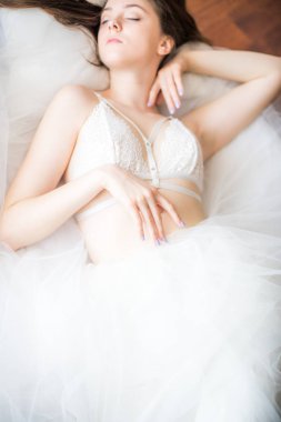 Siyah uzun saçlı sabah evde beyaz bir yatak beyaz dantel büstiyer ve elbise ile genç güzel gelin