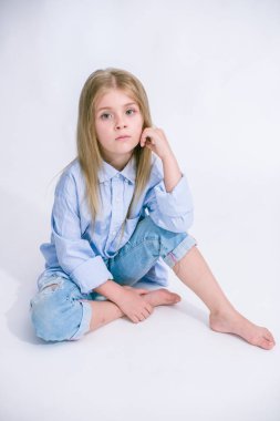 Sarı saçlı beyaz bir arka planda Studio kot pantolon giysili güzel şık küçük kızla