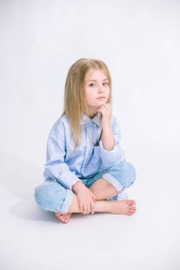 Sarı saçlı beyaz bir arka planda Studio kot pantolon giysili güzel şık küçük kızla