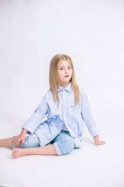 Sarı saçlı beyaz bir arka planda Studio kot pantolon giysili güzel şık küçük kızla