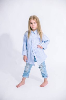 Sarı saçlı beyaz bir arka planda Studio kot pantolon giysili güzel şık küçük kızla