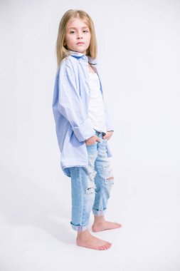 Sarı saçlı beyaz bir arka planda Studio kot pantolon giysili güzel şık küçük kızla