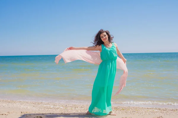 Young girl on the beach in summer in a beautiful dress with a flying scarf — Stock Photo, Image