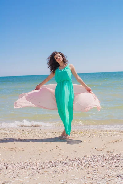 Jong meisje op het strand in de zomer in een mooie jurk met een vliegende sjaal — Stockfoto