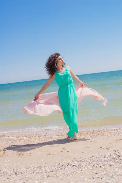 Young girl on the beach in summer in a beautiful dress with a flying scarf — Stock Photo, Image