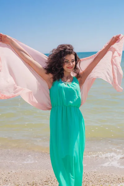 Νεαρό κορίτσι στην παραλία το καλοκαίρι σε ένα όμορφο φόρεμα με ένα ιπτάμενο κασκόλ — Φωτογραφία Αρχείου