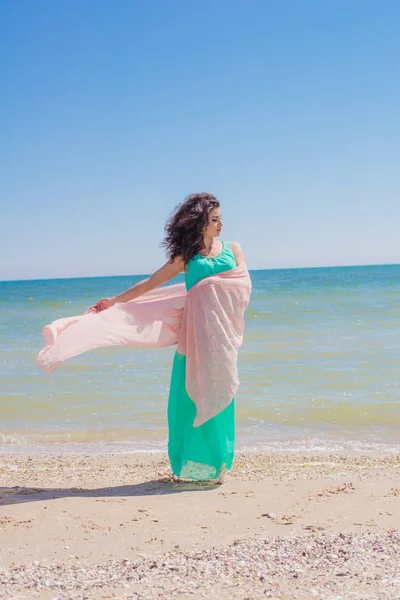 Young girl on the beach in summer in a beautiful dress with a flying scarf — Stock Photo, Image